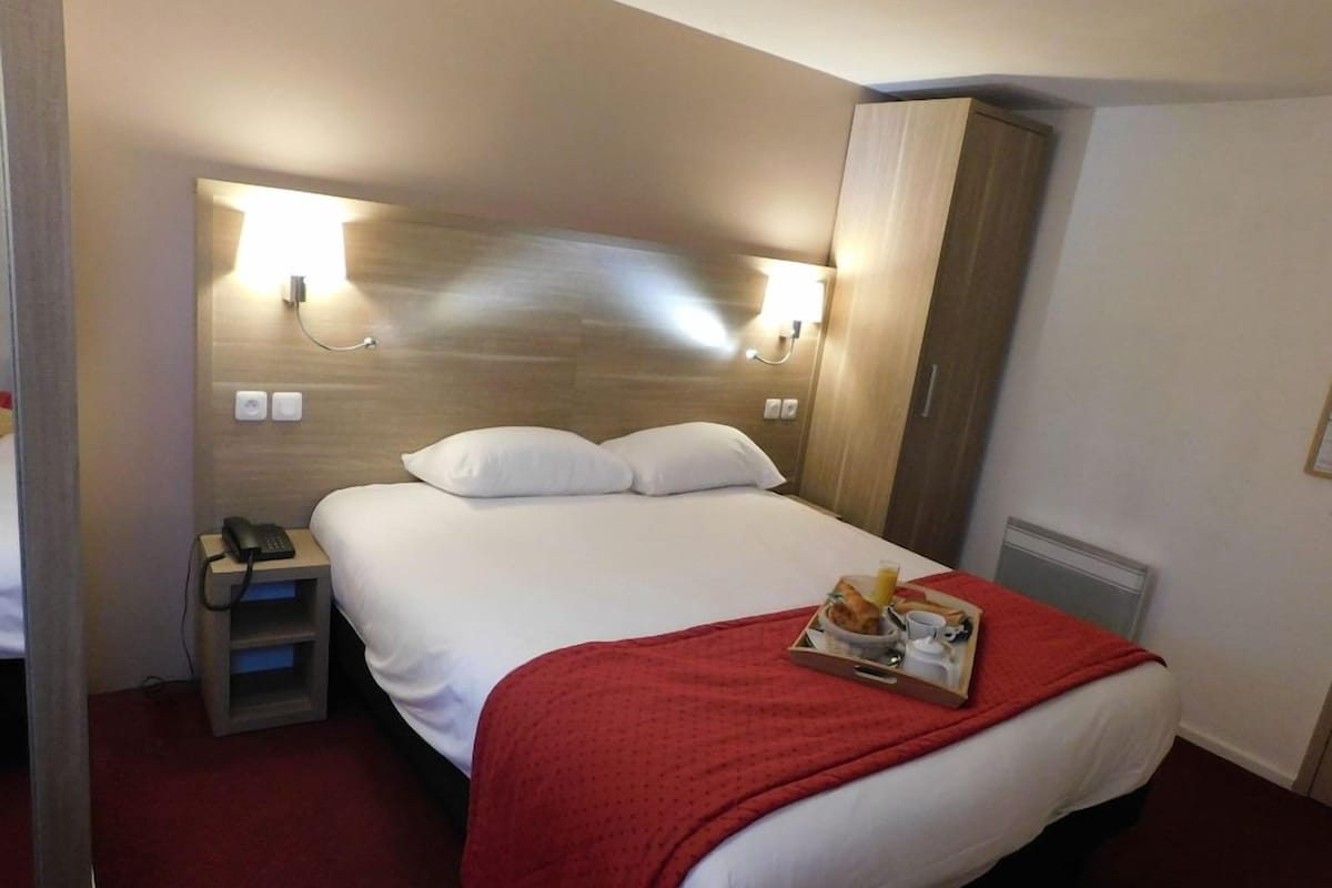 Une chambre d’hôtel avec un lit, une table de chevet avec un téléphone, un plaid rouge et un plateau avec des articles pour le petit-déjeuner.