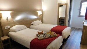 Une chambre d’hôtel avec deux lits, chacun recouvert d’une couverture rouge, un plateau avec des articles pour le petit-déjeuner et des lampes de chevet.