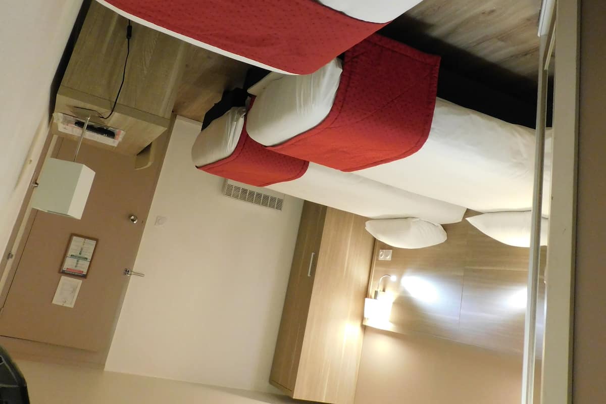 A hotel room with a bed, a desk, and a bathroom visible in the background.
