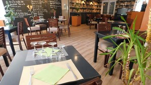 Un restaurant avec des tables et des chaises en bois, un menu écrit à la craie sur un tableau noir et une plante en pot.