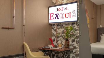 Habitación de hotel con una cama, un escritorio con una silla, una planta en maceta y un letrero que dice "Hotel Exquis".