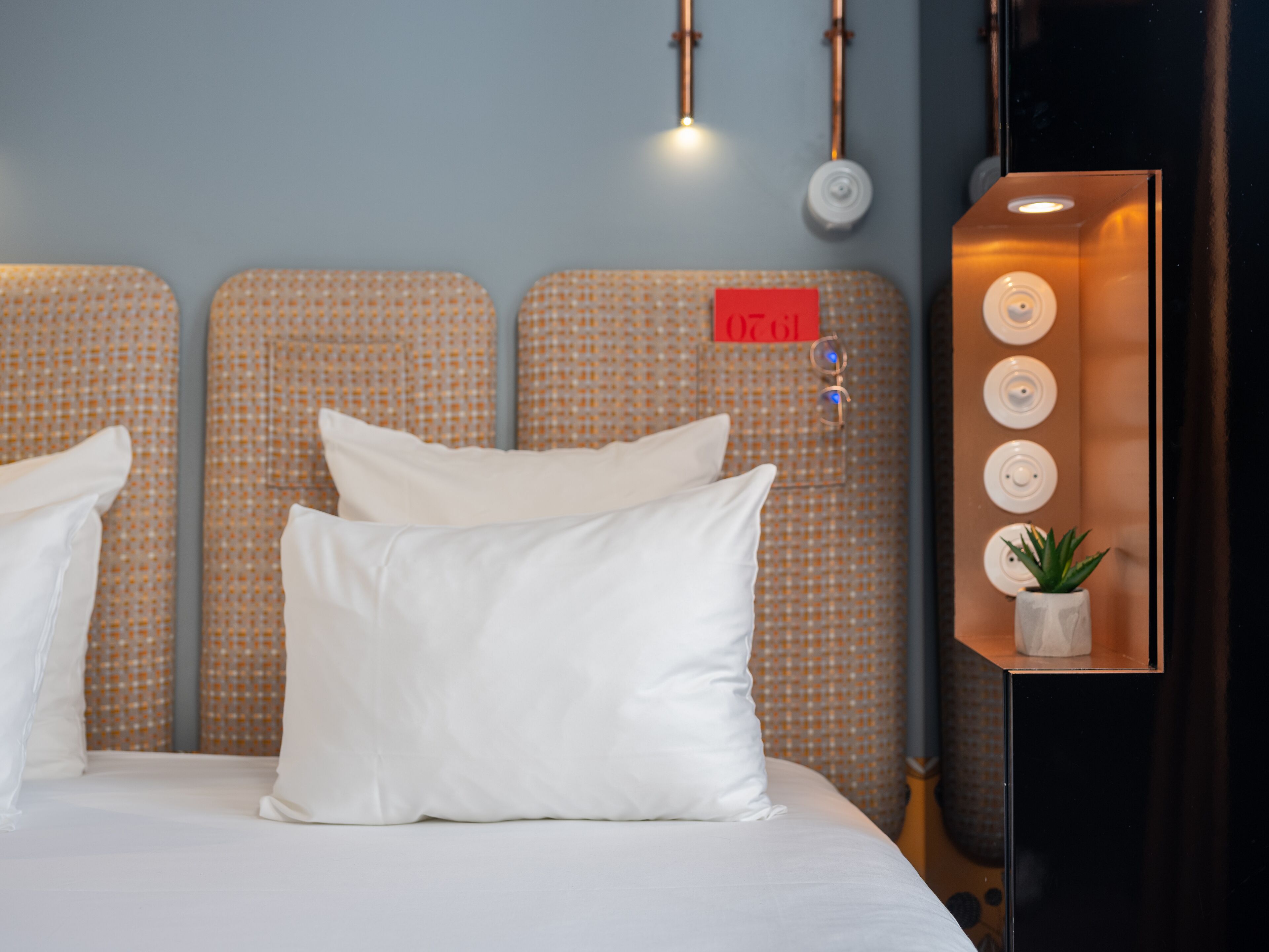 Una cama bien tendida con almohadas blancas y un cabecero con un letrero rojo.