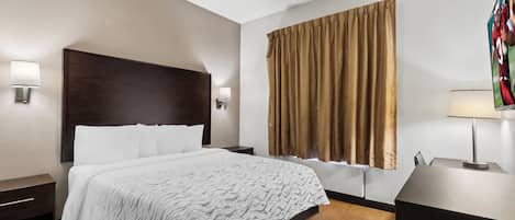 A hotel room with a large bed, two bedside tables, a nightstand, a window with curtains, and a wall-mounted TV.