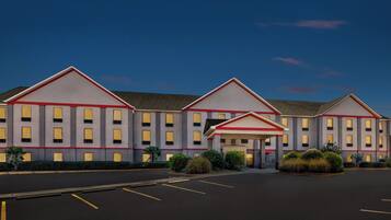A multi-story hotel with a symmetrical facade, a central entrance, and a parking lot in front.