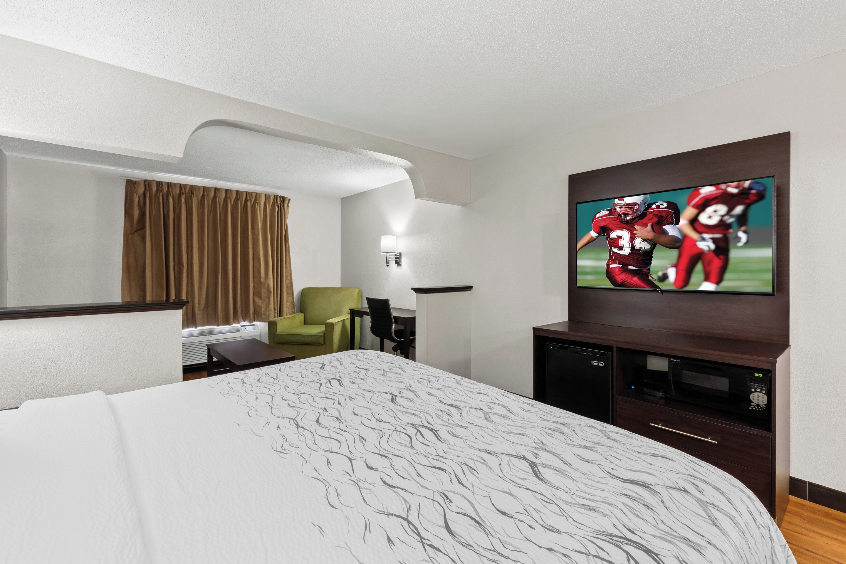 Habitación de hotel con cama, televisor montado en la pared, escritorio y una silla.