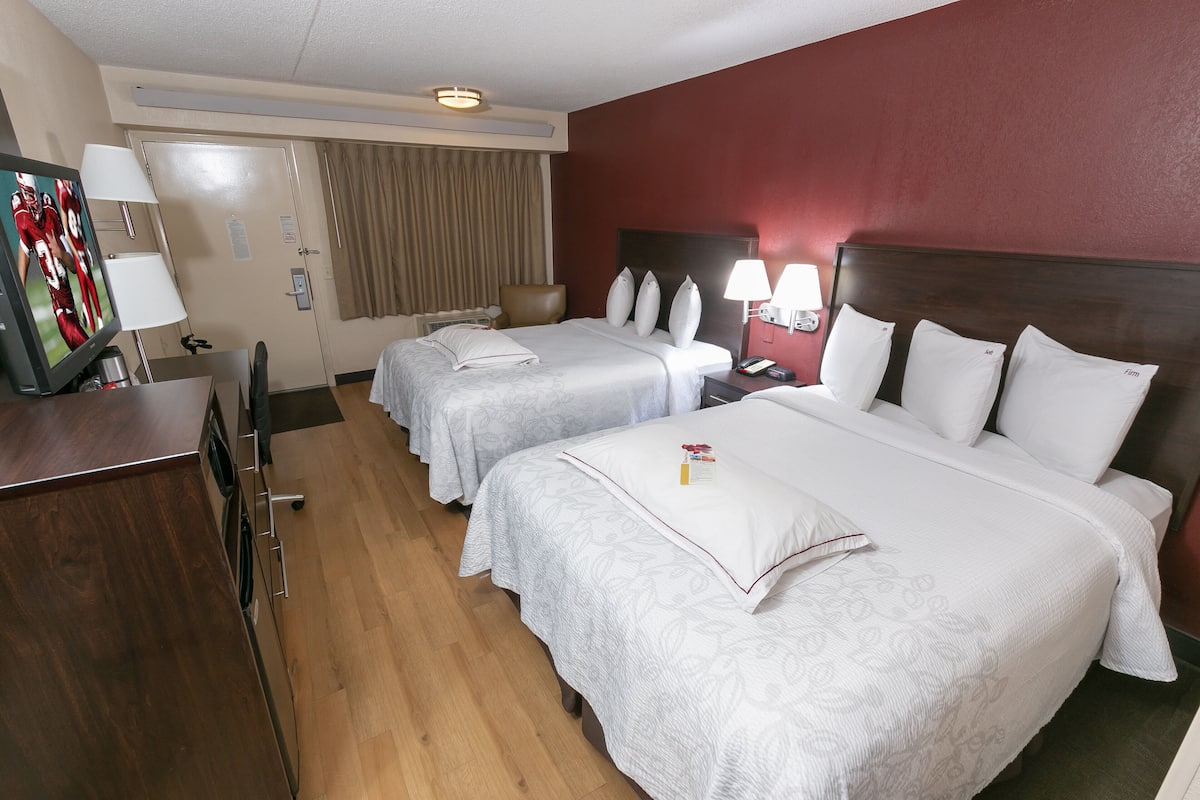 A hotel room with two beds, a desk with a TV, and a bathroom visible through an open door.