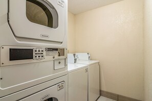 Een wasserette met een voorlader wasmachine en droger, een bedieningspaneel met verschillende instellingen, en een wandgedragen droger.