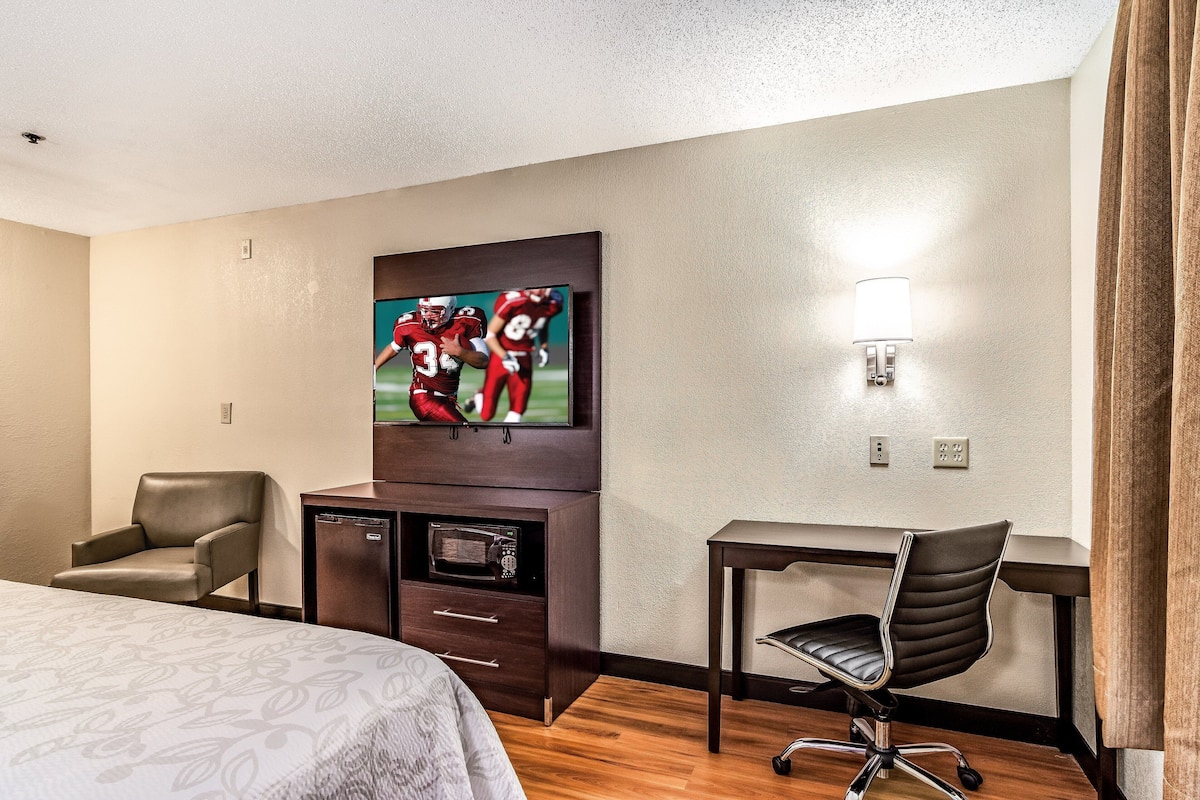 A hotel room with a bed, a desk, a chair, a TV, and a microwave.