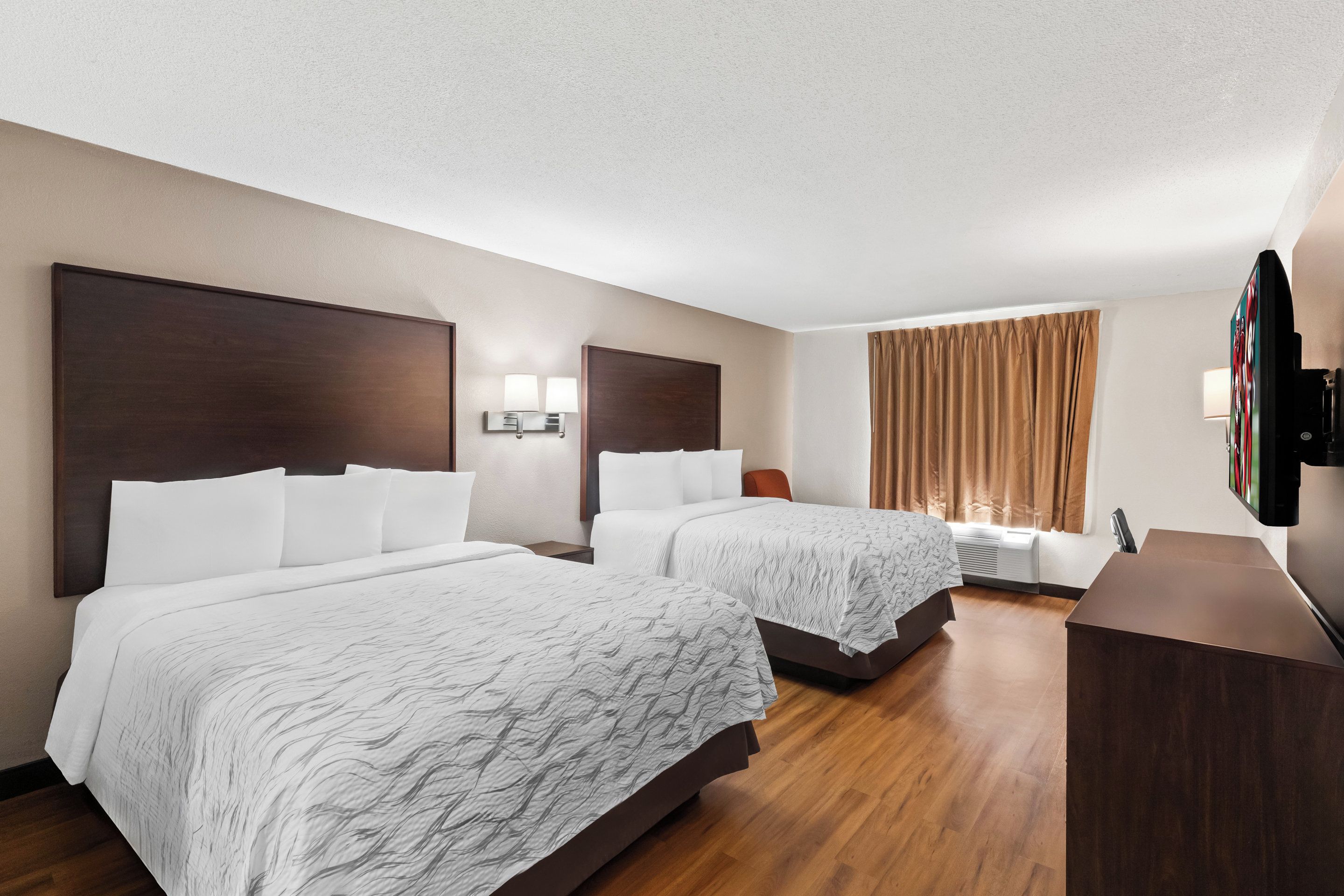 A hotel room with two beds, a flat-screen TV, a desk, and a window with curtains.