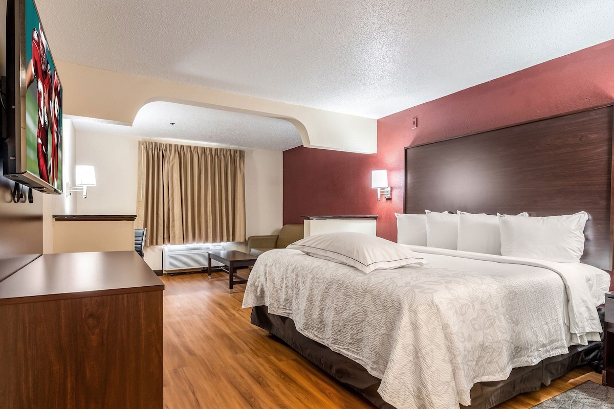A hotel room with a bed, a desk, a chair, a TV, and a window with curtains.