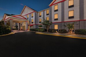 A multi-story hotel with a covered entrance, multiple windows, and a landscaped driveway.