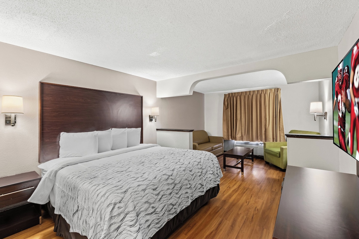 A hotel room with a large bed, a desk, a sofa, and a TV.