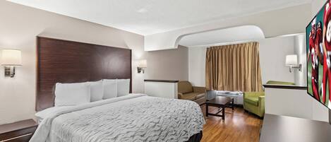 A hotel room with a large bed, a desk, a sofa, and a TV.