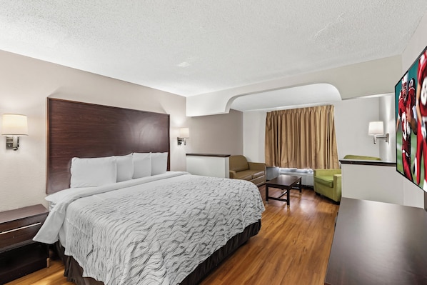 A hotel room with a large bed, a desk, a sofa, and a TV.