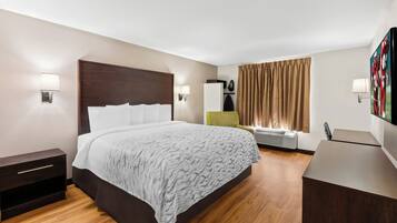 Habitación de hotel con cama, mesitas de noche, escritorio, silla, televisor y ventana con cortinas.