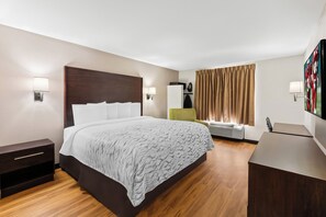 A hotel room with a bed, bedside tables, a desk, a chair, a TV, and a window with curtains.