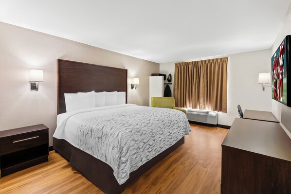 A hotel room with a bed, bedside tables, a desk, a chair, a TV, and a window with curtains.