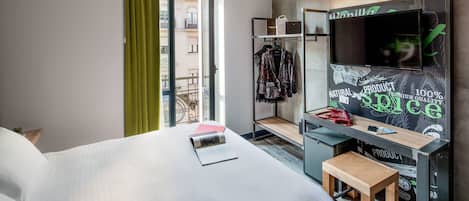 Habitación de hotel con cama, escritorio con computadora, televisor y vista al exterior.