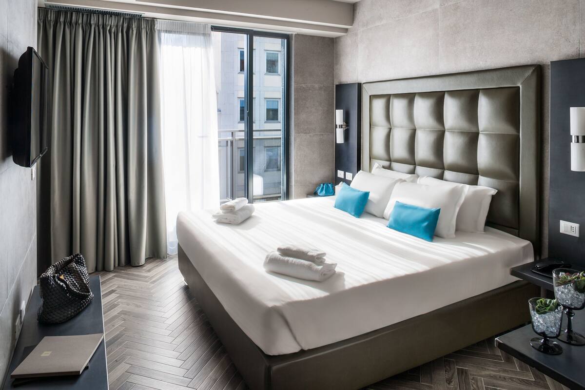 Camera d'albergo moderna con un letto grande, una TV a schermo piatto, una scrivania e vista sulla città dalla finestra.