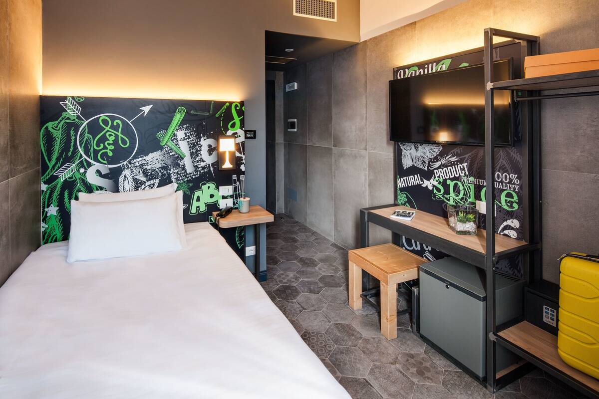 A hotel room with a bed, a desk, a chair, and a wardrobe.