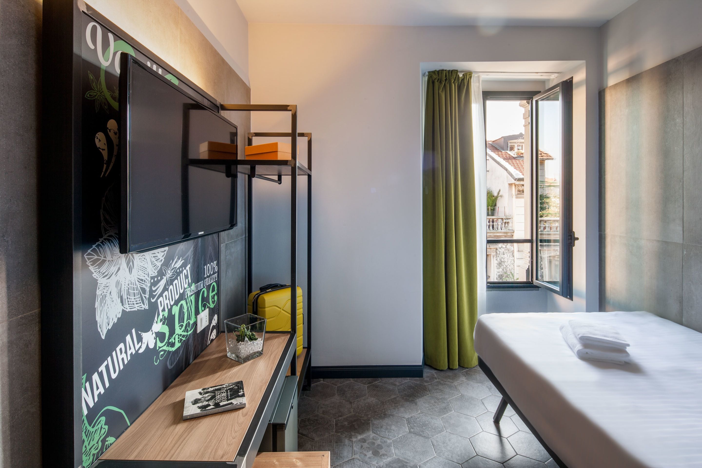 Habitación de hotel con literas, un escritorio, una computadora portátil, una maleta y una ventana con cortinas.