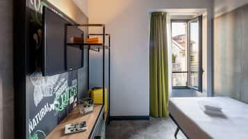 Habitación de hotel con literas, un escritorio, una computadora portátil, una maleta y una ventana con cortinas.