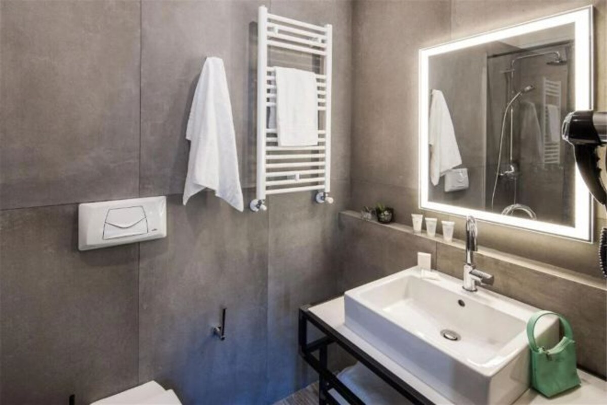 A modern bathroom with a white sink, a towel rack, a mirror with lights, and a shower.