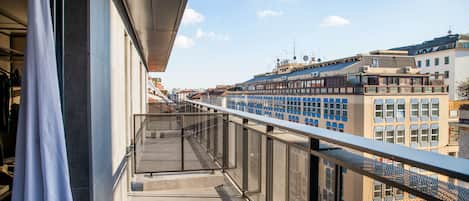 A balcony with a metal railing overlooking a cityscape with buildings and a clear sky.