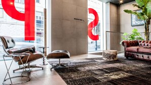 A modern lobby with a large red 'P' sign, a leather chair, a red sofa, and a plant. - Spice Hotel Milano (Milan)