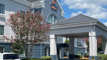 Un hotel Comfort Suites con entrada cubierta, zona de estacionamiento y un árbol con flores rosadas.