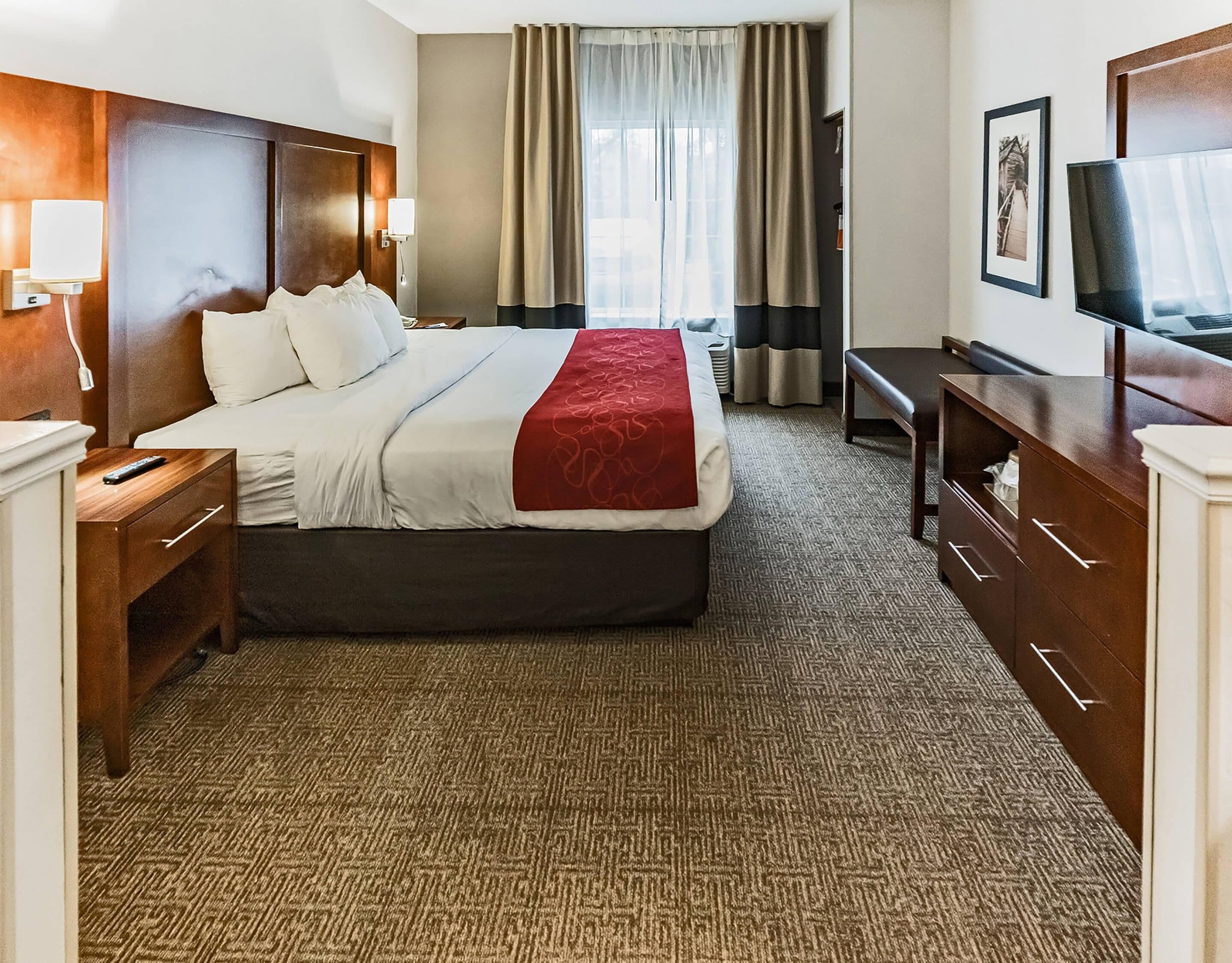 A hotel room with a bed, bedside tables, a desk, a chair, a television, and a window with curtains.