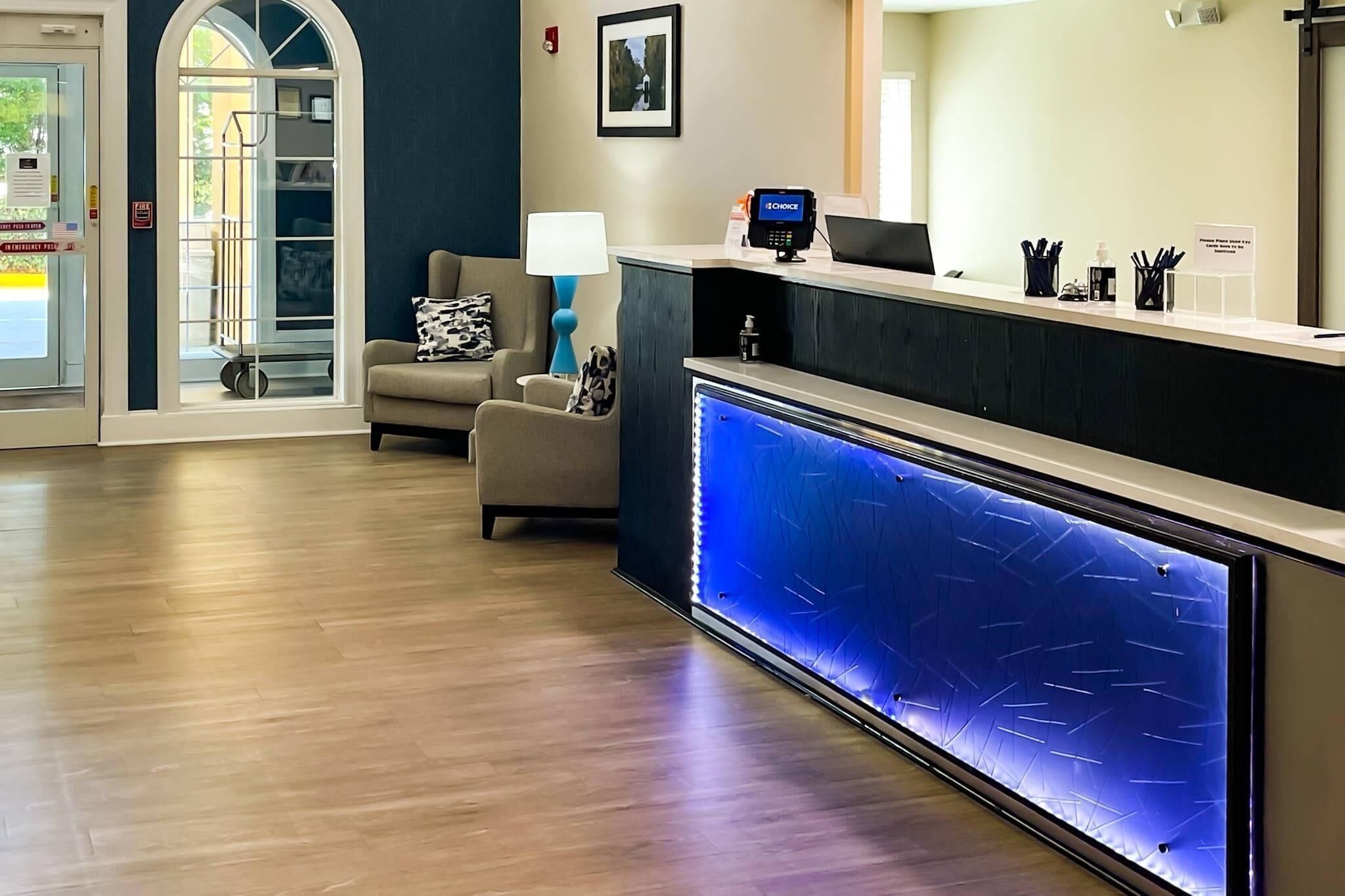A reception area with a counter, a blue-lit water feature, a chair with a patterned pillow, and a lamp.