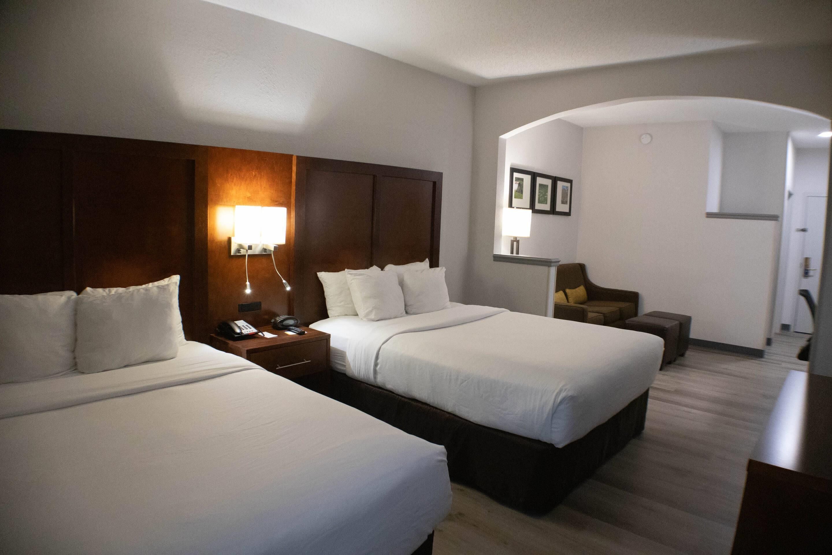 A hotel room with two beds, a desk, a chair, and a lamp.