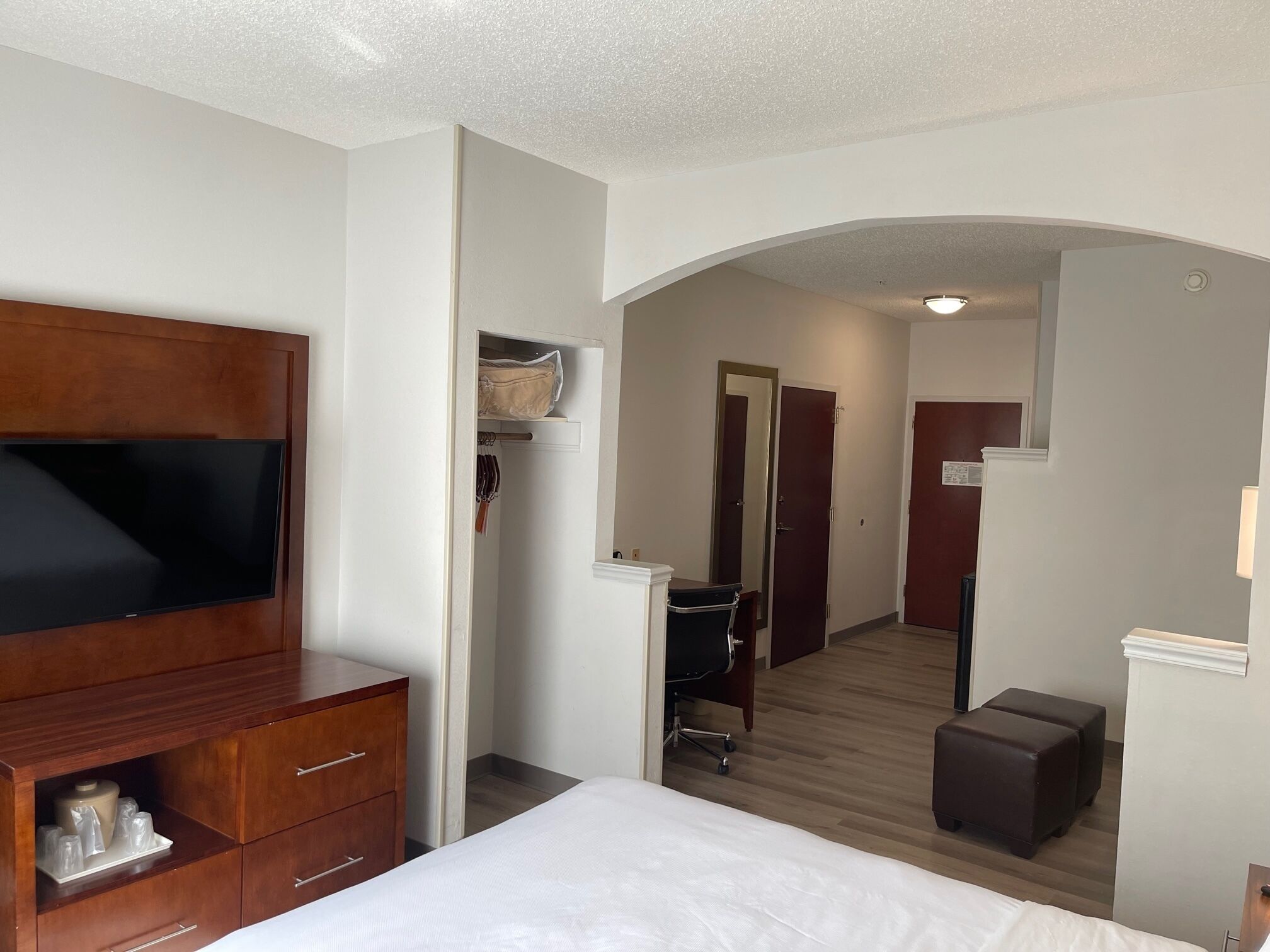 Habitación de hotel con cama, televisión, cómoda de madera, armario y escritorio con silla.
