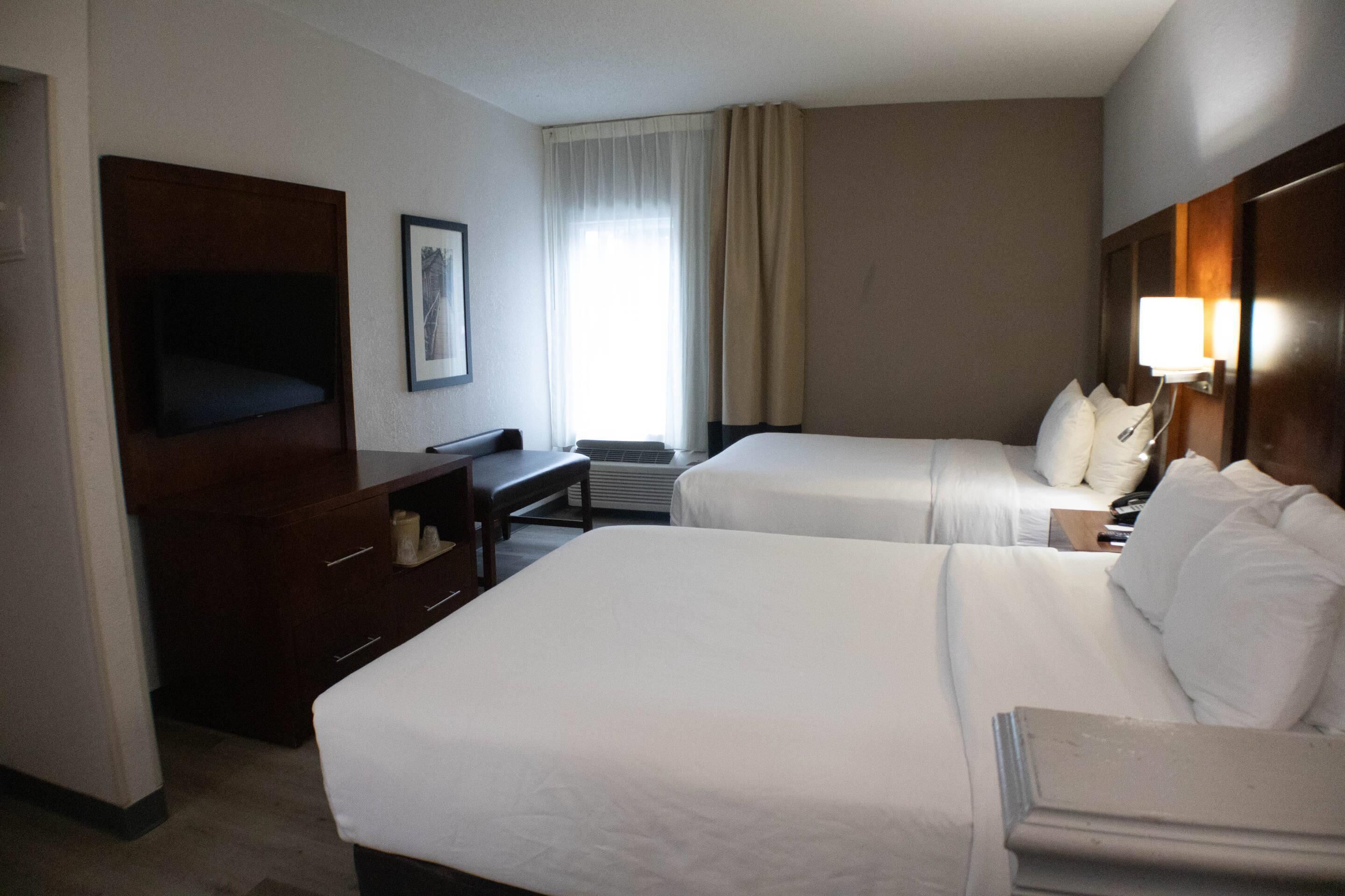 A hotel room with two beds, a desk, a chair, a television, and a window with curtains.