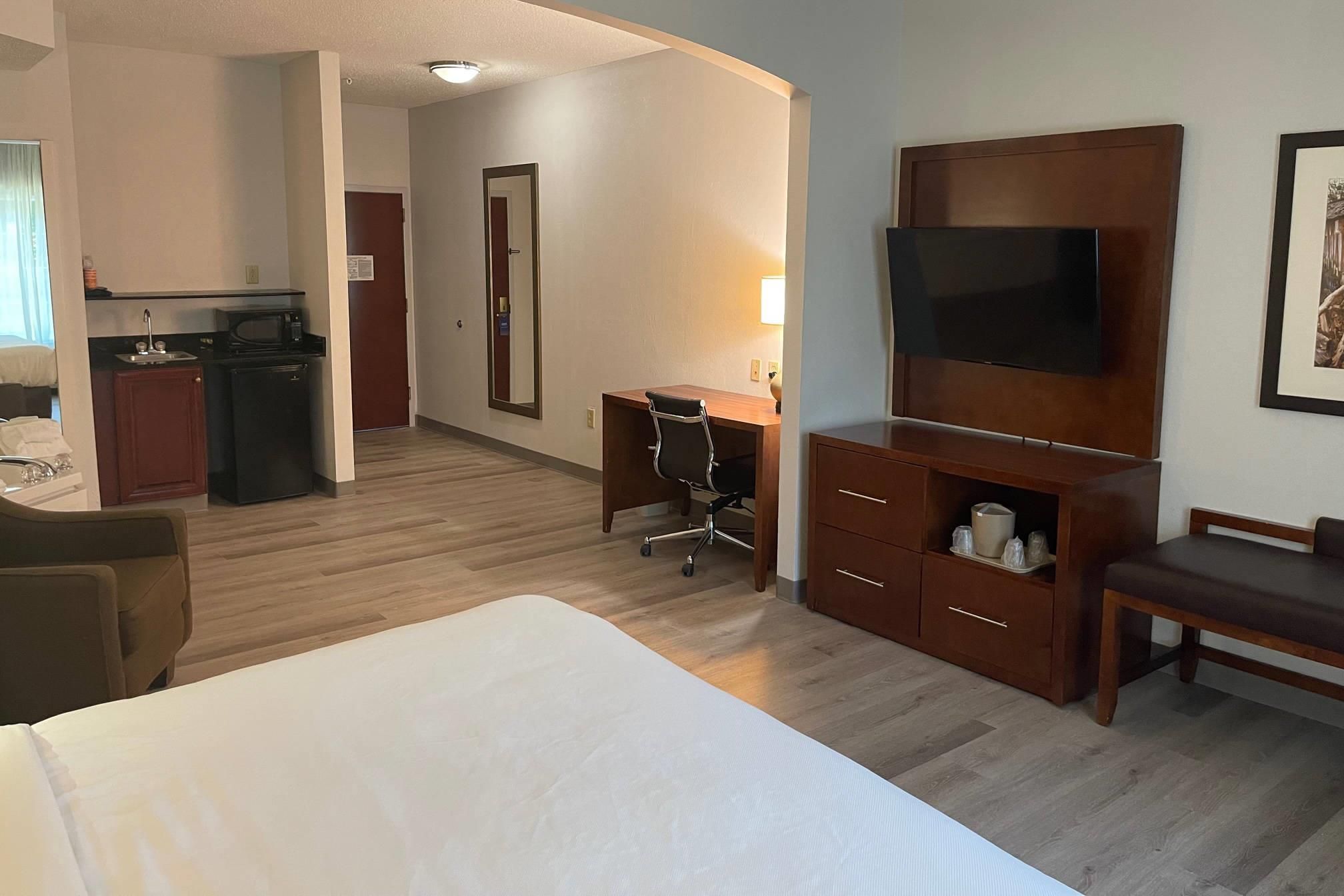 A hotel room with a bed, a desk, a television, a dresser, and a kitchenette.