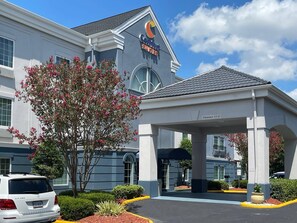 A Comfort Suites hotel with a covered entrance, a parking area, and a tree with pink flowers.