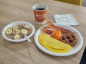 Un plato de desayuno con waffles, tocino, rodajas de naranja y un tazón de cereal con rodajas de plátano.