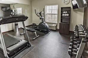 A gym with a treadmill, elliptical, dumbbells, and a wall clock.