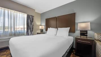 Habitación de hotel con una cama grande, dos mesitas de noche con lámparas, una ventana con cortinas traslúcidas y una alfombra estampada.