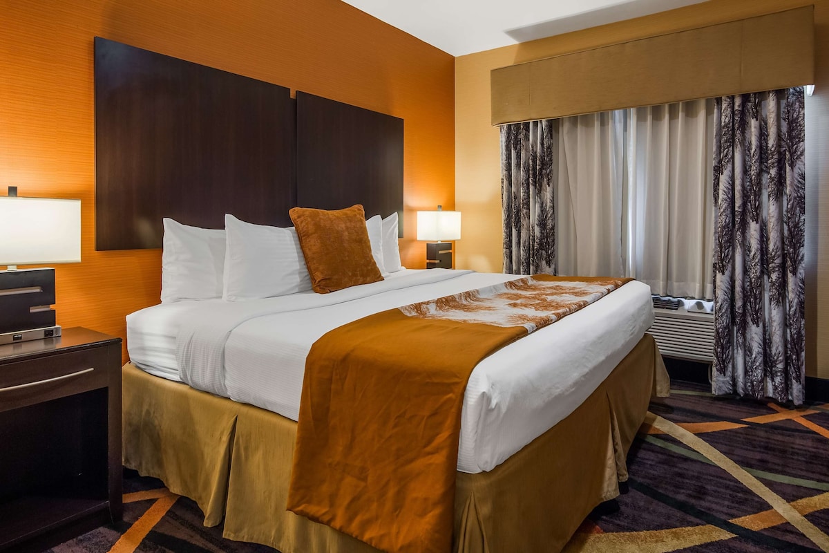 Quarto de hotel com uma cama grande, televisão de tela plana, escrivaninha com luminária e cômoda.