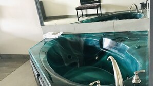 Ein Badezimmer mit einer großen, dunkel gefliesten Badewanne, einem Spiegel und einem Waschbecken.