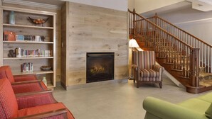 Ein geräumiges Wohnzimmer mit Kamin, einem gestreiften Sessel und einer Treppe mit Holzwertungen.
