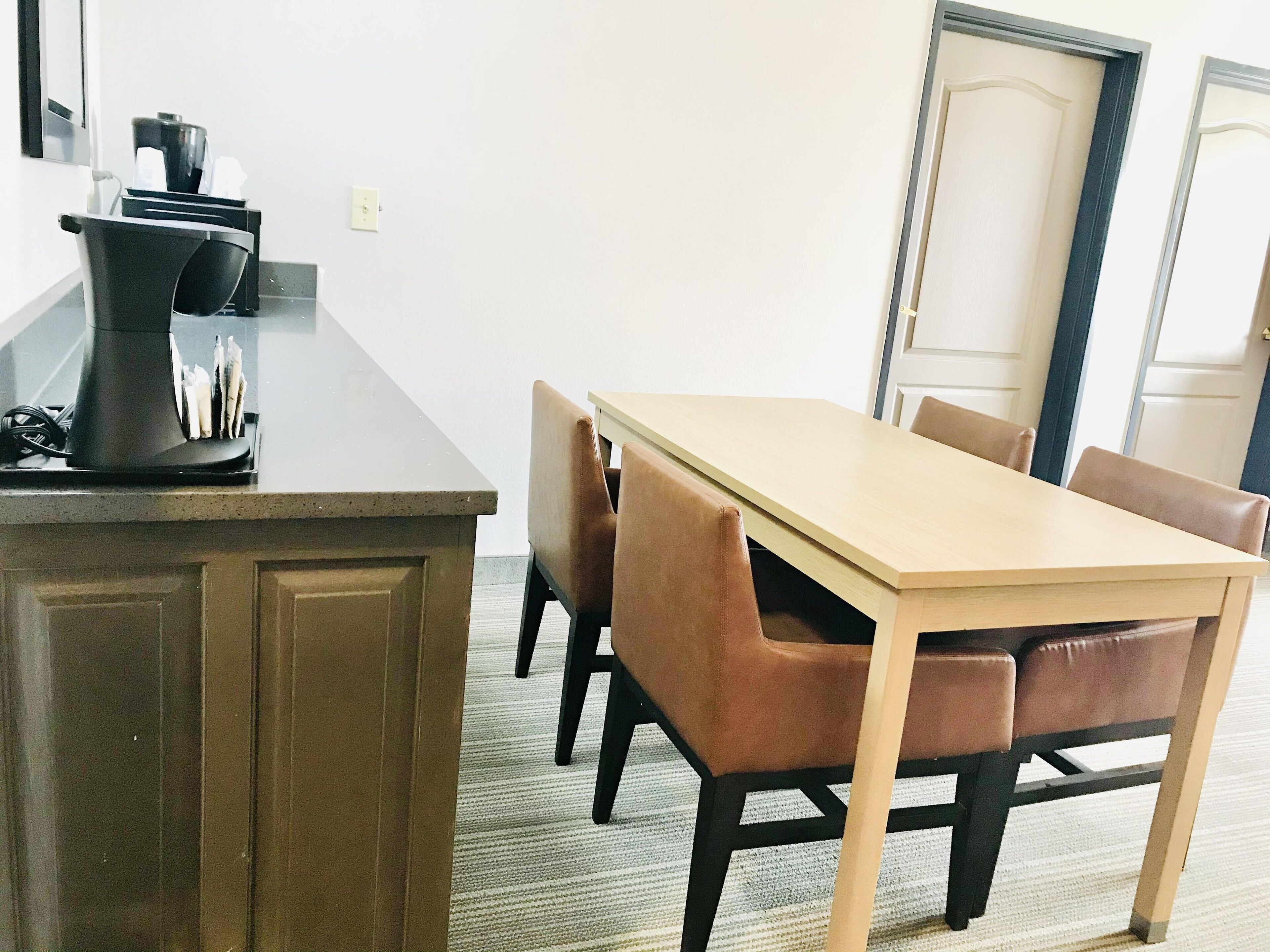 A dining area with a wooden table and four chairs, a coffee machine, and a trash bin.