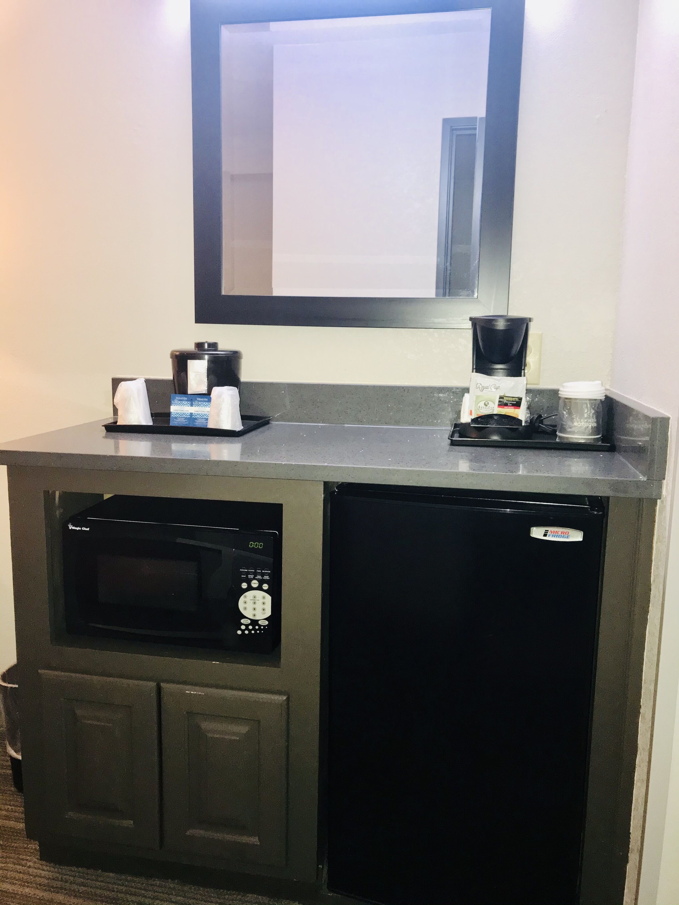 Una kitchenette compacta con microondas, cafetera y un refrigerador pequeño.