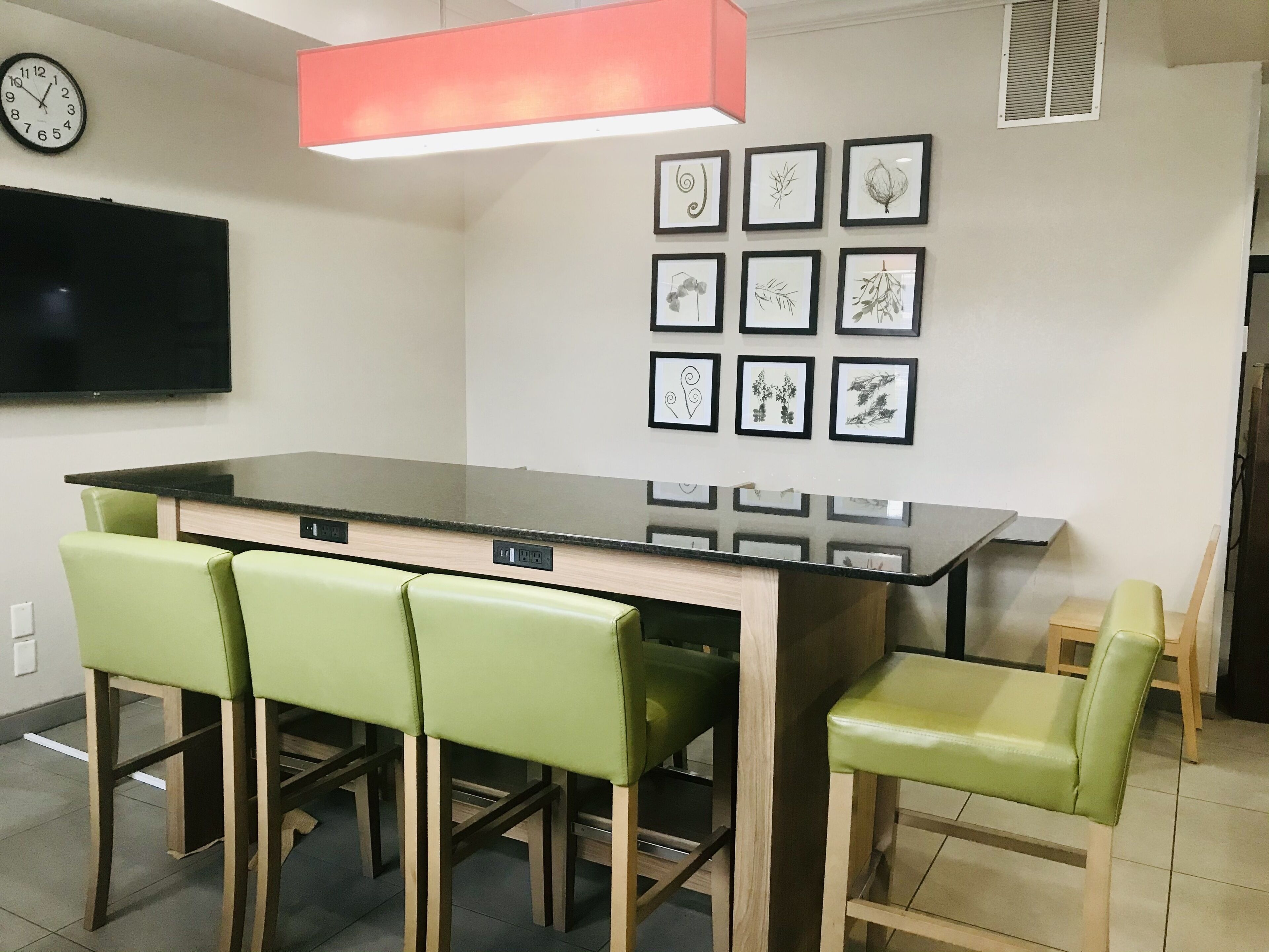A modern kitchen with a central island, green bar stools, a flat-screen TV, and framed botanical artwork on the wall.