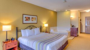 A hotel room with a bed, bedside lamps, a bathroom with a bathtub, and a small wooden cabinet. - Country Inn & Suites by Radisson, Crystal Lake, IL (Crystal Lake)