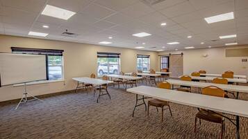 A conference room with multiple tables and chairs, a whiteboard, and large windows with blinds.