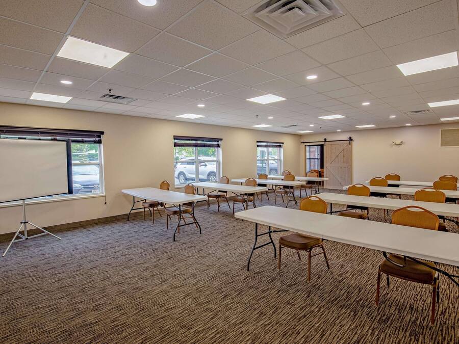 A conference room with multiple tables and chairs, a whiteboard, and large windows with blinds.