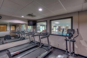 Un gimnasio con cintas de correr, una máquina elíptica y un espejo grande.